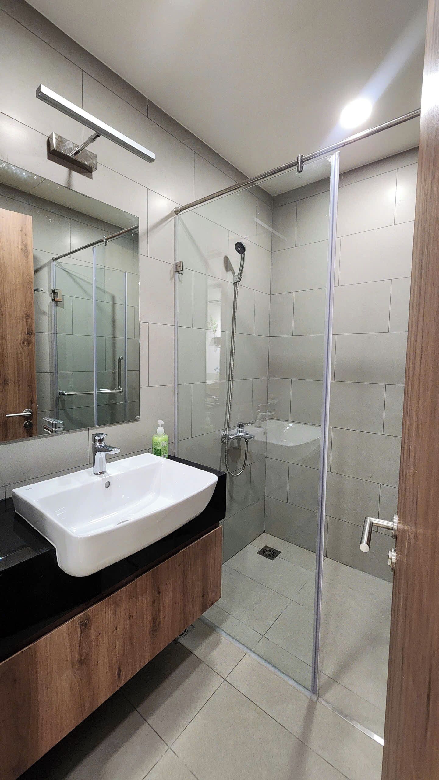 Un bagno moderno con box doccia in vetro, lavandino bianco e uno specchio grande.