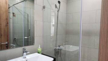 Un bagno moderno con box doccia in vetro, lavandino bianco e uno specchio grande.