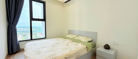 A bedroom with a bed, a nightstand, a window with a view of buildings, and an air conditioning unit.
