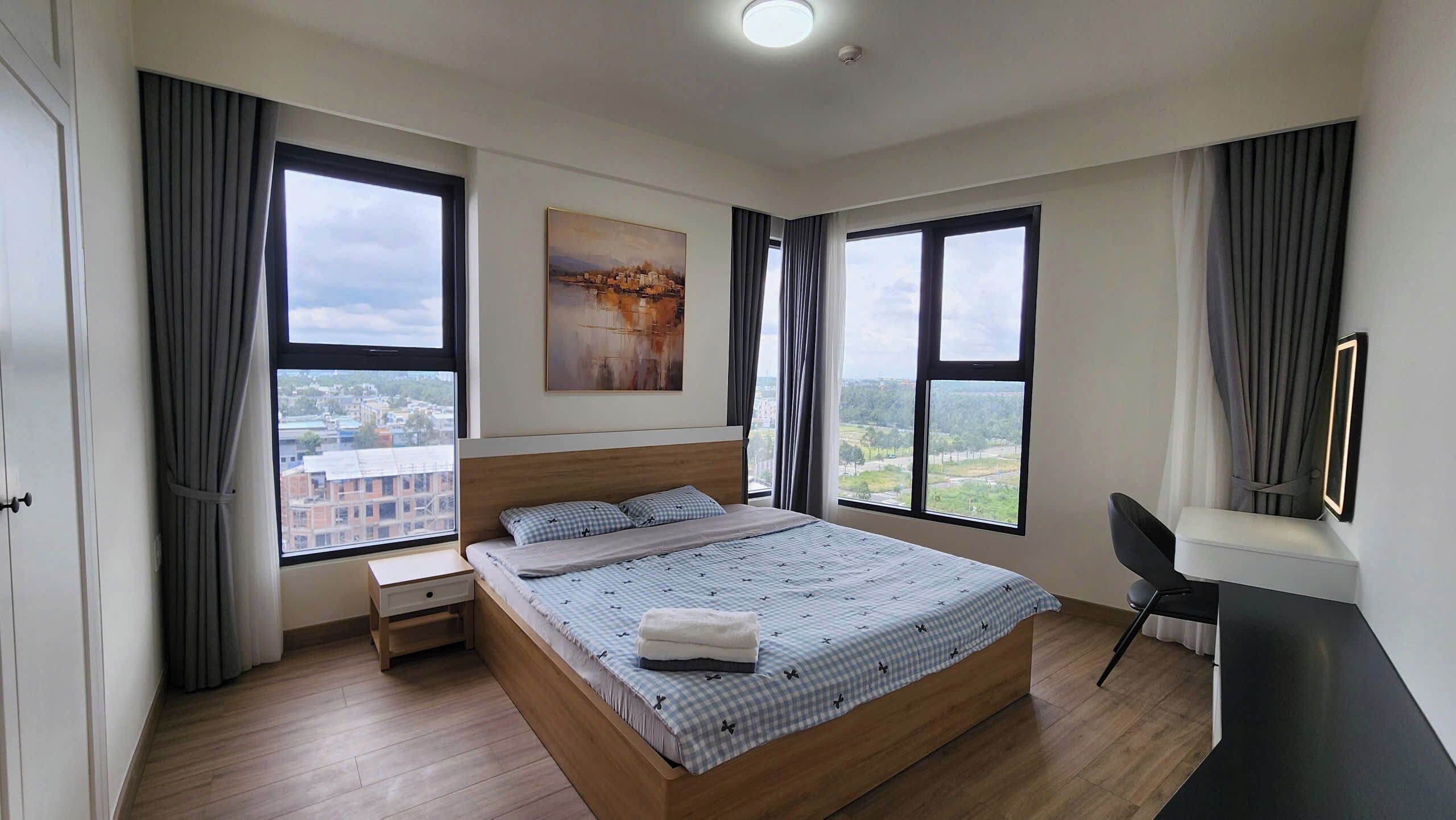 Une chambre moderne dotée d’un grand lit, d’un bureau et de deux fenêtres donnant sur la ville.