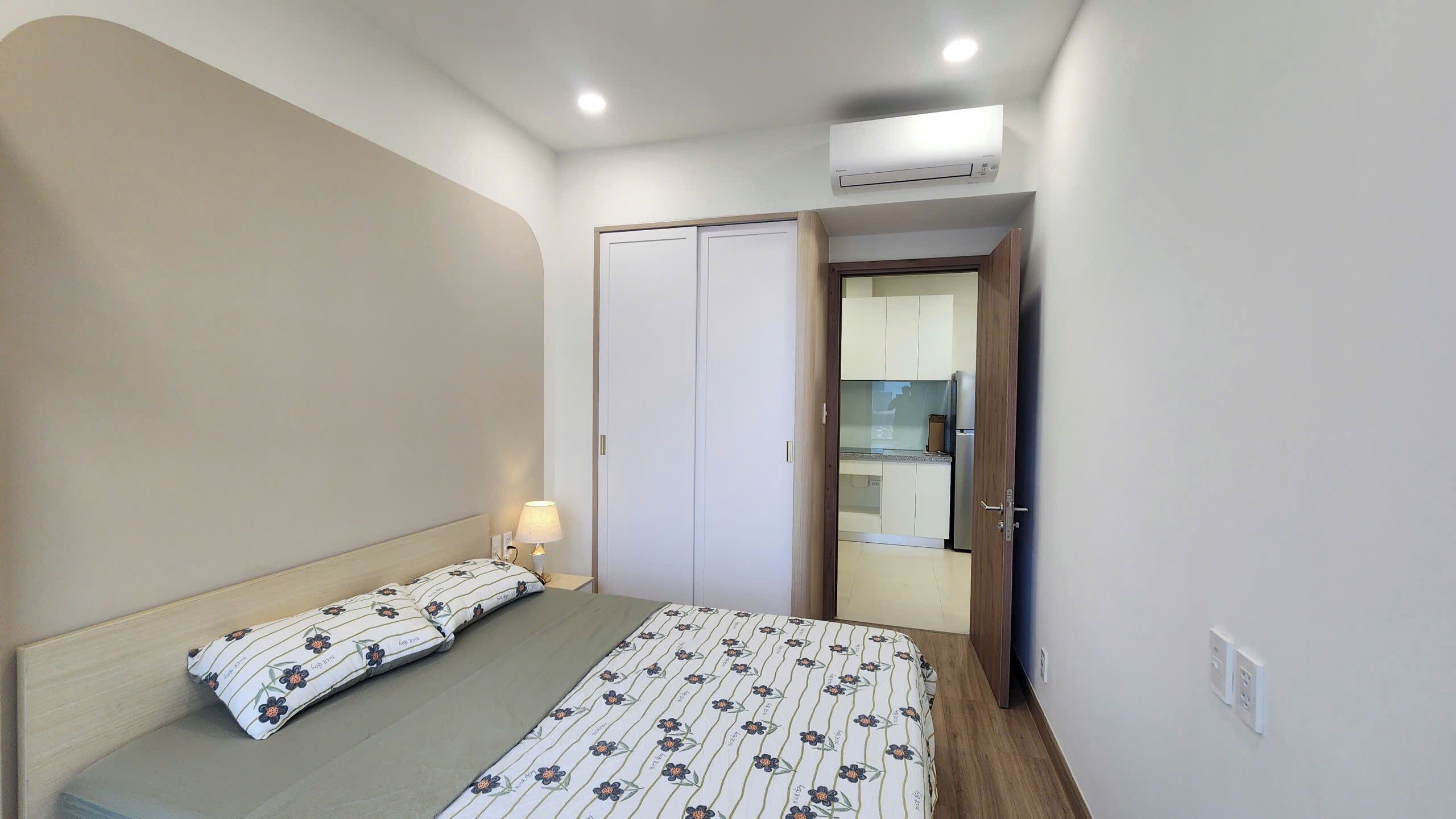 A bedroom with a bed, a bedside lamp, a wardrobe, and an air conditioning unit.