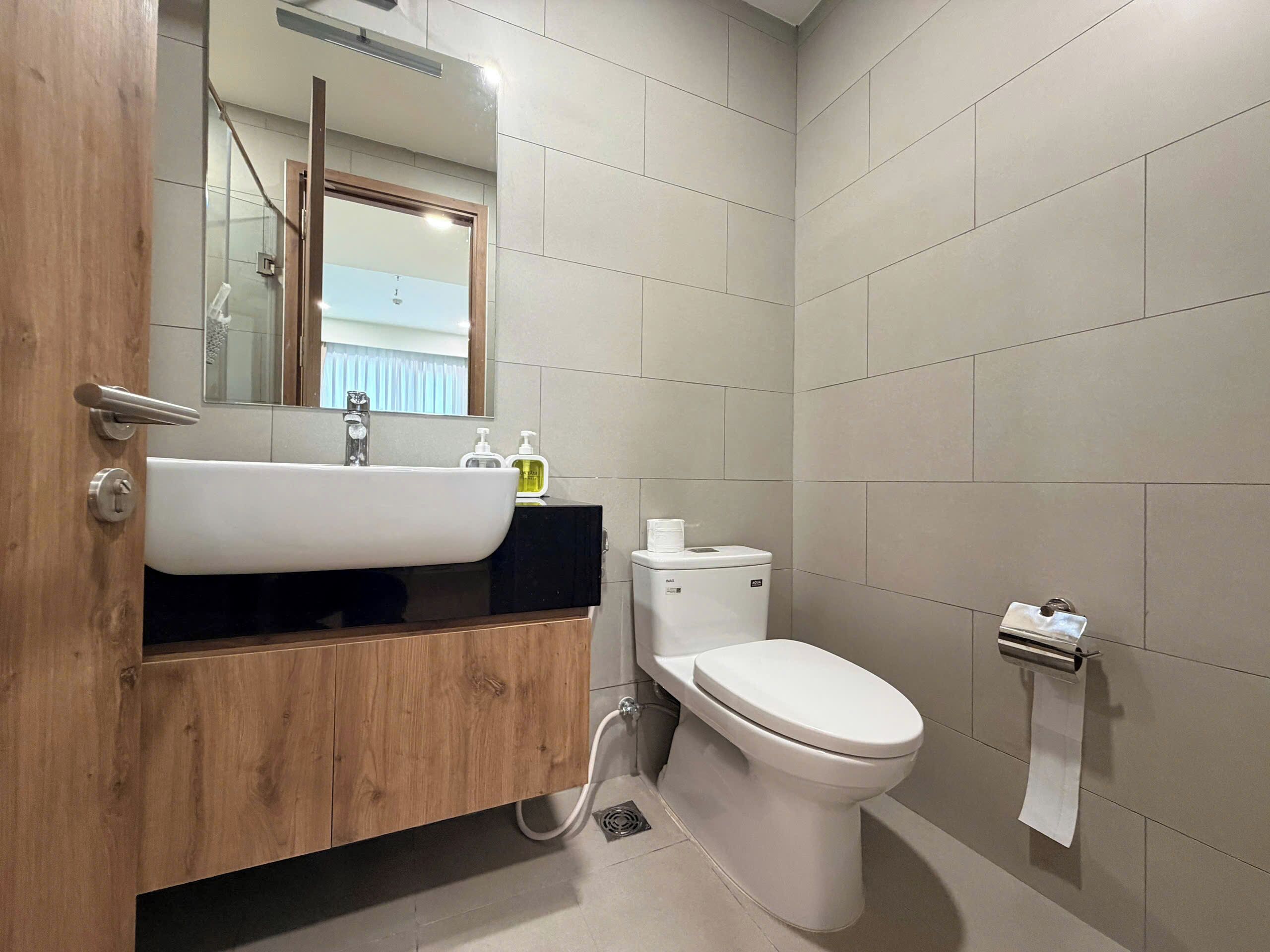 Une salle de bain avec un meuble-lavabo en bois, un lavabo blanc, des toilettes et un distributeur de serviettes.
