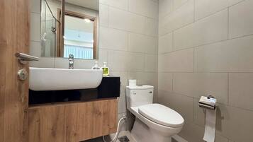 Une salle de bain avec un meuble-lavabo en bois, un lavabo blanc, des toilettes et un distributeur de serviettes.