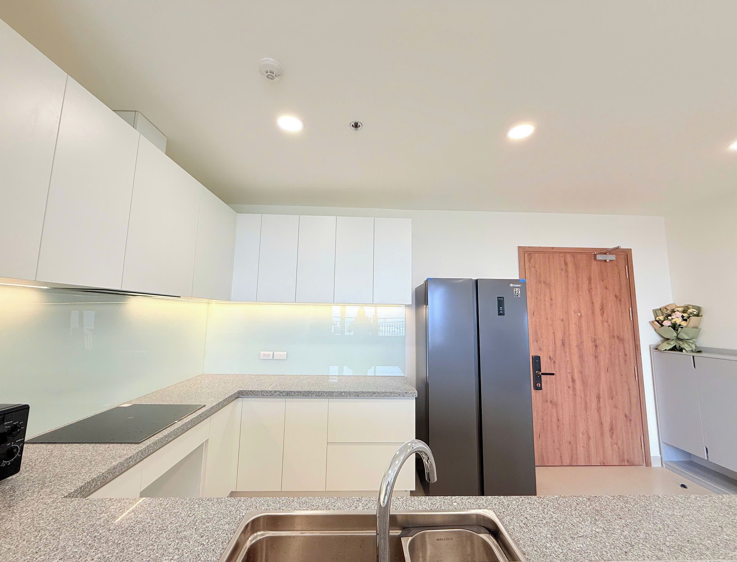 A modern kitchen with white cabinets, a stainless steel sink, a black refrigerator, and a wooden door.