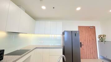A modern kitchen with white cabinets, a stainless steel sink, a black refrigerator, and a wooden door.