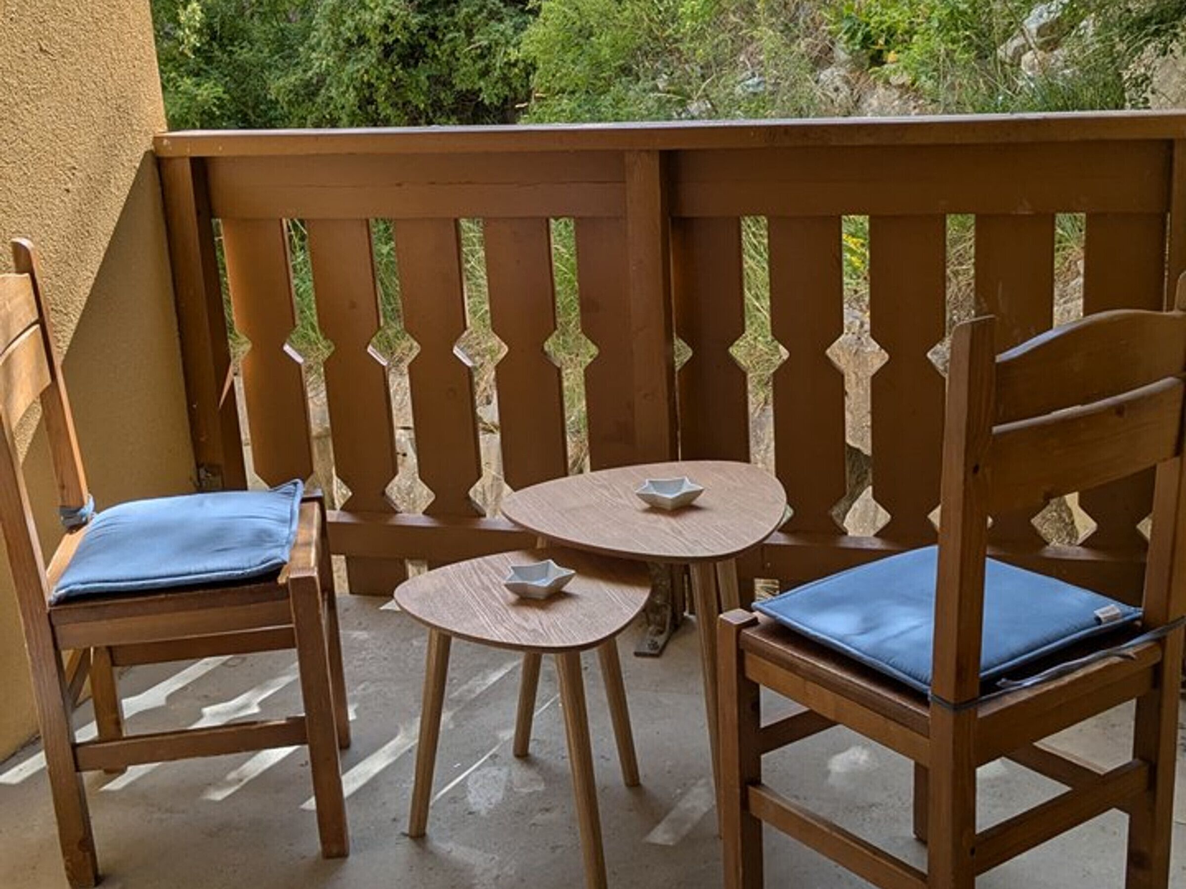 Ein hölzerner Balkon mit zwei Stühlen und einem kleinen Tisch, versehen mit einer verzierten Reling.