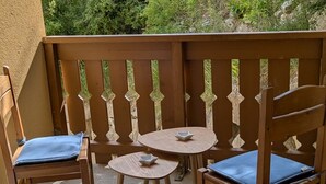 Ein hölzerner Balkon mit zwei Stühlen und einem kleinen Tisch, versehen mit einer verzierten Reling.