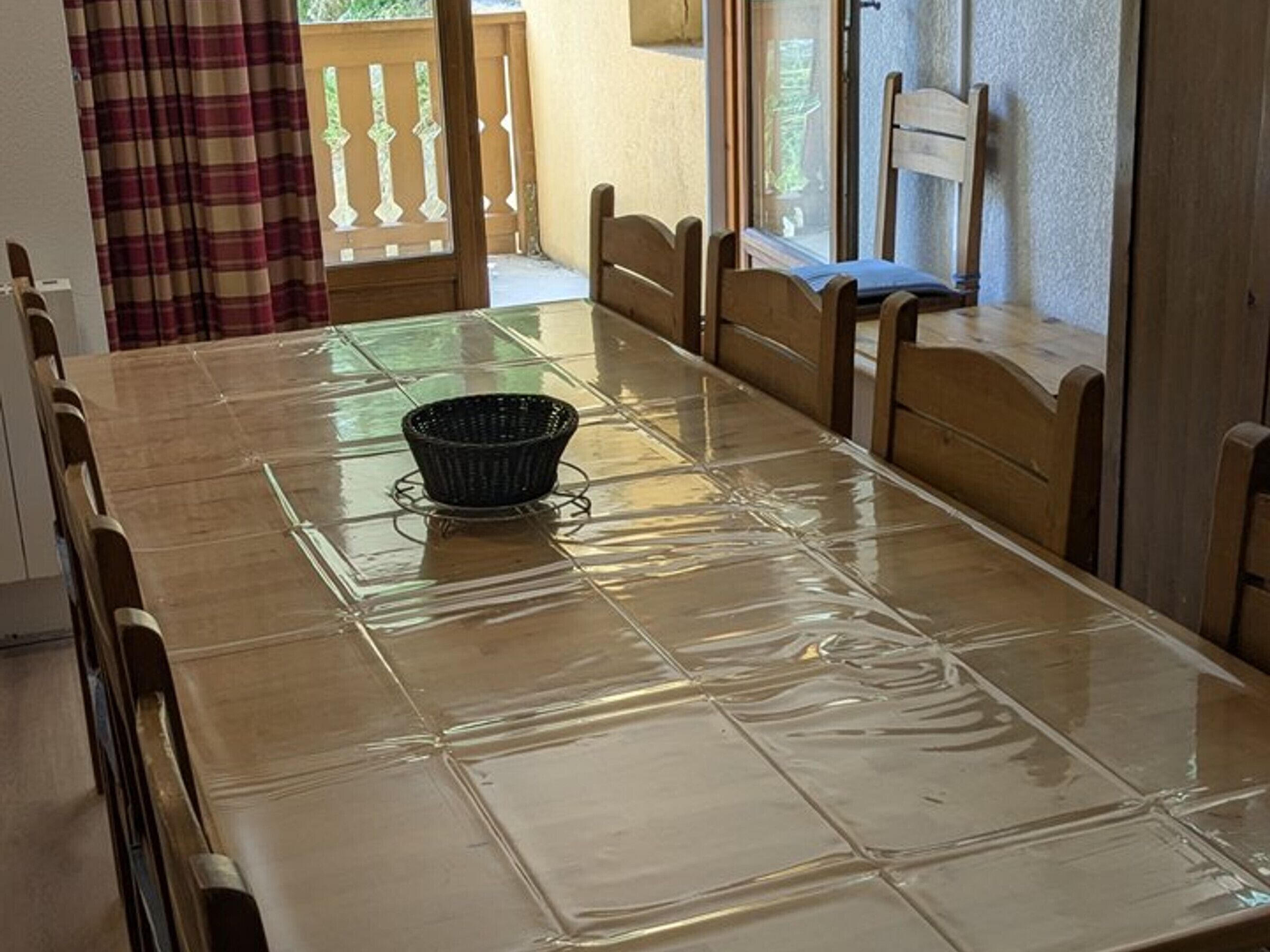 A dining table with a plastic cover, wooden chairs, and a basket in the center.