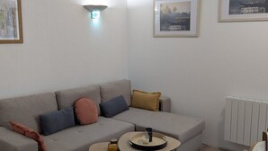 Ein Wohnzimmer mit einem grauen Sofa, zwei kleinen Beistelltischen und einem gerahmten Bild an der Wand.