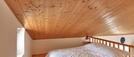 Un dormitorio con techo de madera, una cama con ropa blanca, una mesita de noche y un reloj de pared.