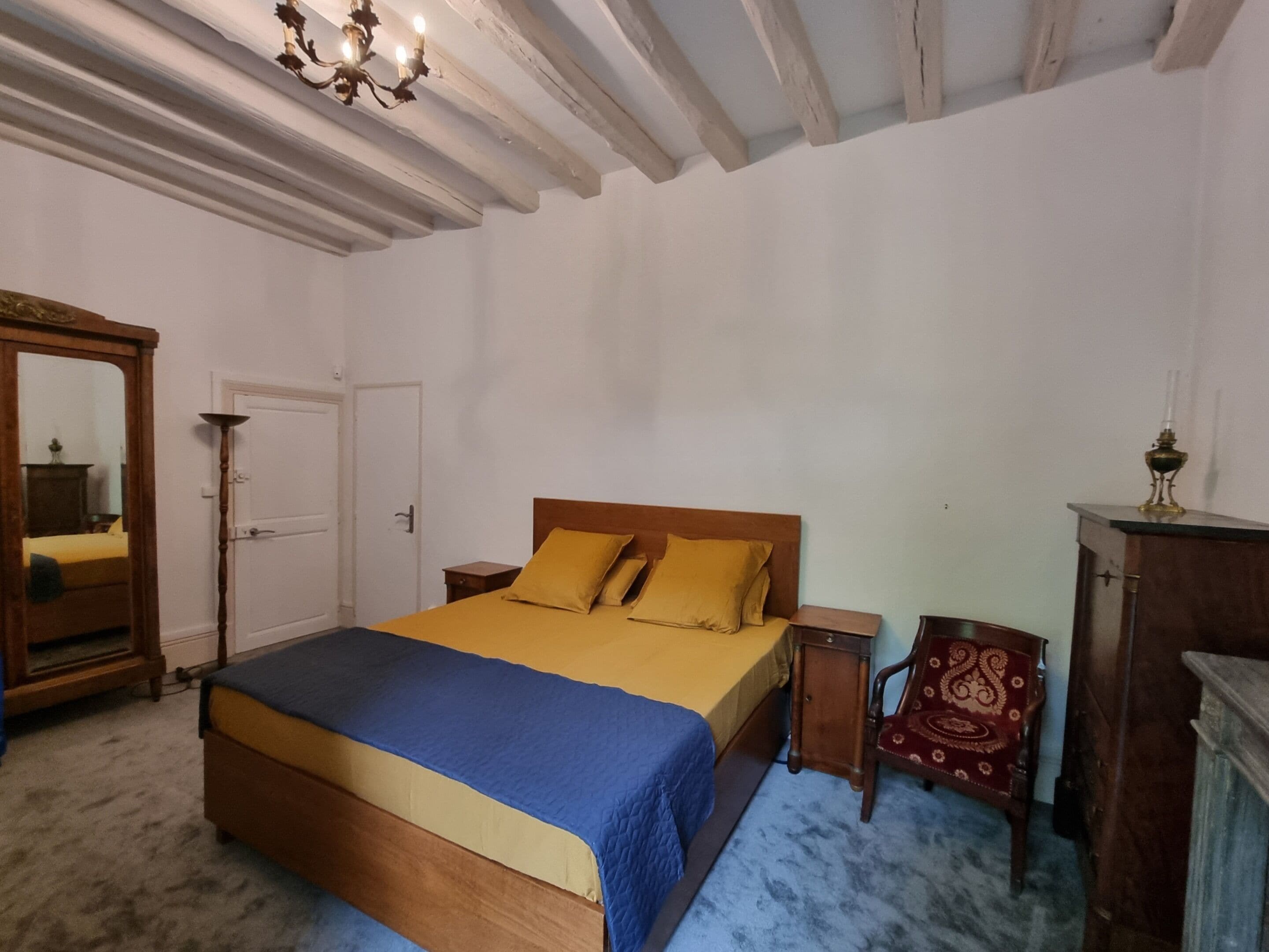 A bedroom with a wooden bed, a nightstand, a mirror, a wardrobe, and a chandelier.