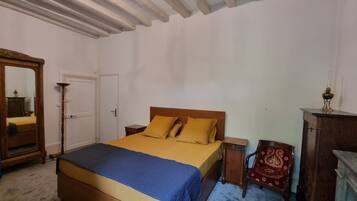 A bedroom with a wooden bed, a nightstand, a mirror, a wardrobe, and a chandelier.