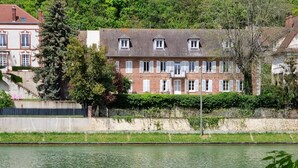 A swan swimming in a calm body of water with a residential area in the background. - Merlin Cottage (Montereau-Fault-Yonne)