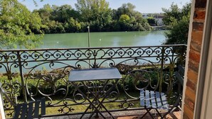 A balcony with a metal railing, a small table, and two chairs, overlooking a green lake with trees and a distant building. - Merlin Cottage (Montereau-Fault-Yonne)
