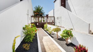 A narrow alleyway with white walls, a gate, and various potted plants. - Apartment 'Romance' with Shared Pool, Private Terrace and Wi-Fi (Puerto del Carmen)
