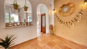 Un pasillo con un cartel que dice 'IBISAVIBE', una araña, cestas colgantes, una decoración mural tejida y un taburete tejido.