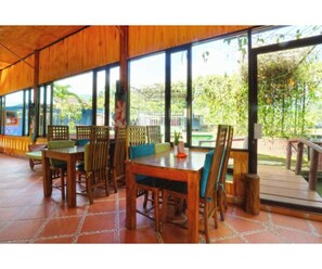 A wooden dining area with large windows and a view of greenery outside. - Belvilla Bogor near Citra Alam Riverside formerly Aries Biru Hotel (Cisarua)