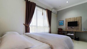 A hotel room with a bed, curtains, a TV mounted on the wall, and a small desk area.