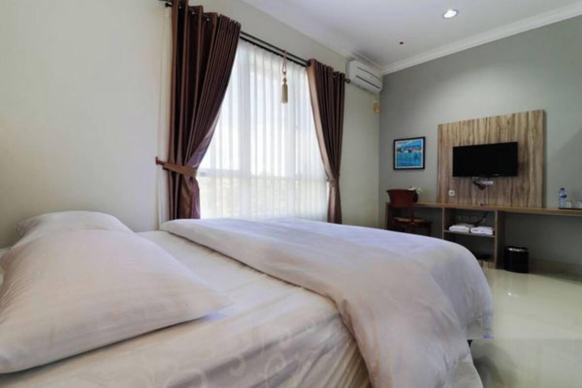 Habitación de hotel con cama, cortinas, televisor montado en la pared y un pequeño escritorio.