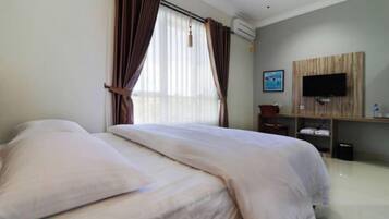 Habitación de hotel con cama, cortinas, televisor montado en la pared y un pequeño escritorio.