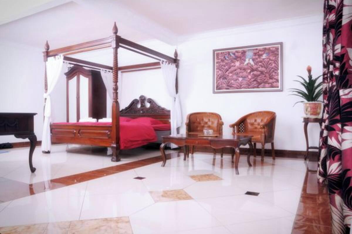 Una cama con dosel con una colcha roja, una mesa de centro de madera, dos sillones tapizados y una obra de arte enmarcada en la pared.