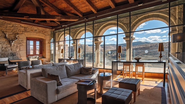 A spacious living room with a large sofa, a coffee table, and a view through arched windows. - Hotel Hospedería Palacio de Allepuz (Allepuz)