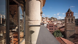 A balcony with a stone column, a view of a town with red-roofed buildings, and a bell tower. - Hotel Hospedería Palacio de Allepuz (Allepuz)