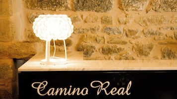 Un mur de pierre sur lequel est fixée une lampe blanche, le tout posé sur une surface noire portant l’inscription « Camino Real ».