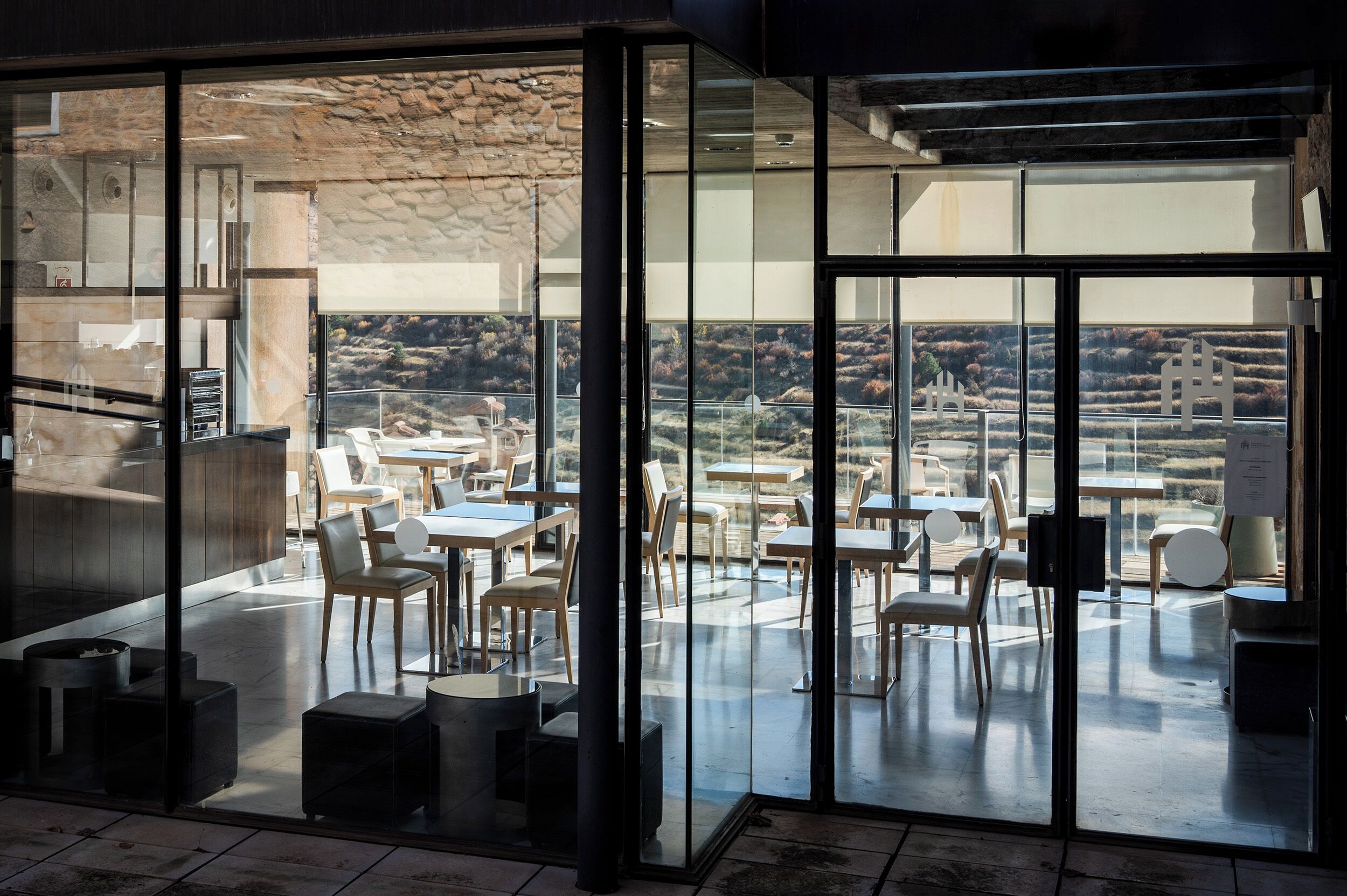 Un comedor moderno con paredes de vidrio, una pared de piedra y vistas al campo.