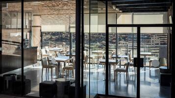Un comedor moderno con paredes de vidrio, una pared de piedra y vistas al campo.