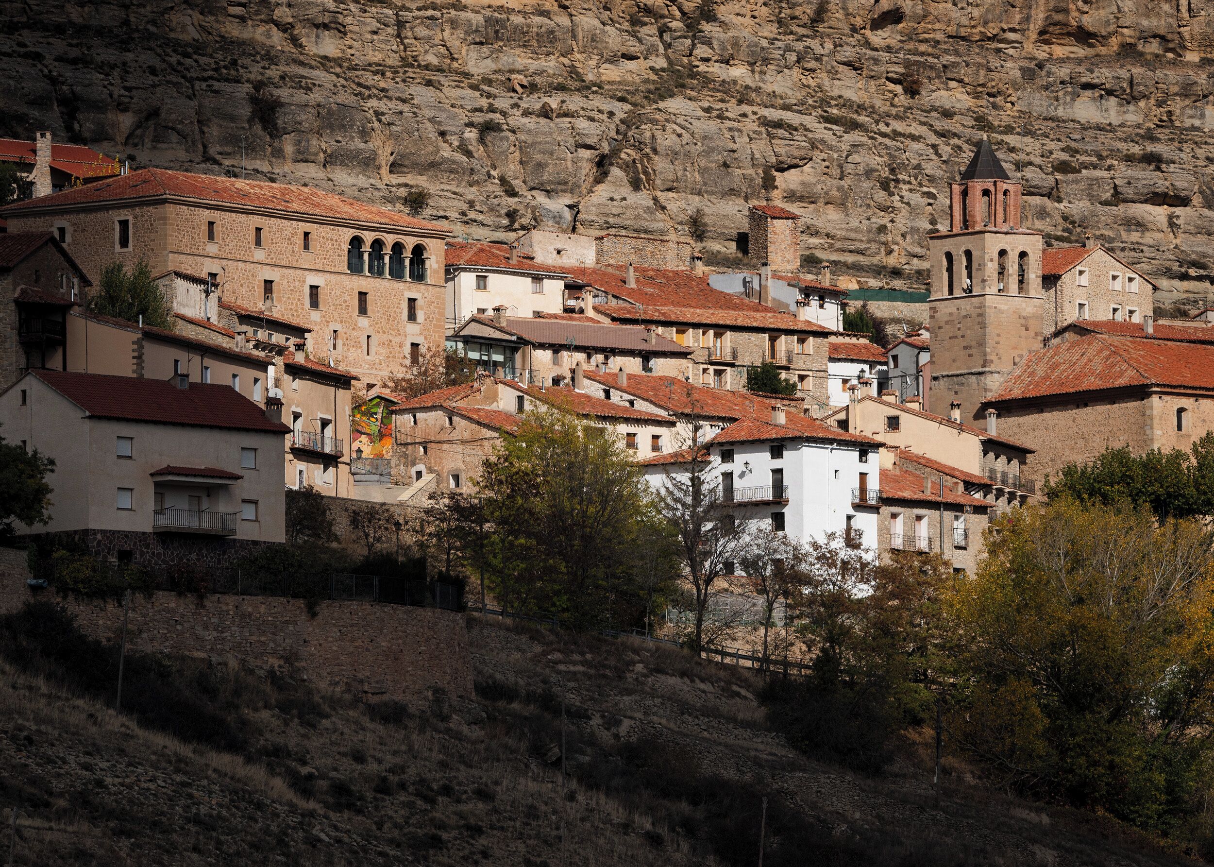 Un pueblo en la ladera con edificios de piedra, una iglesia y un campanario.