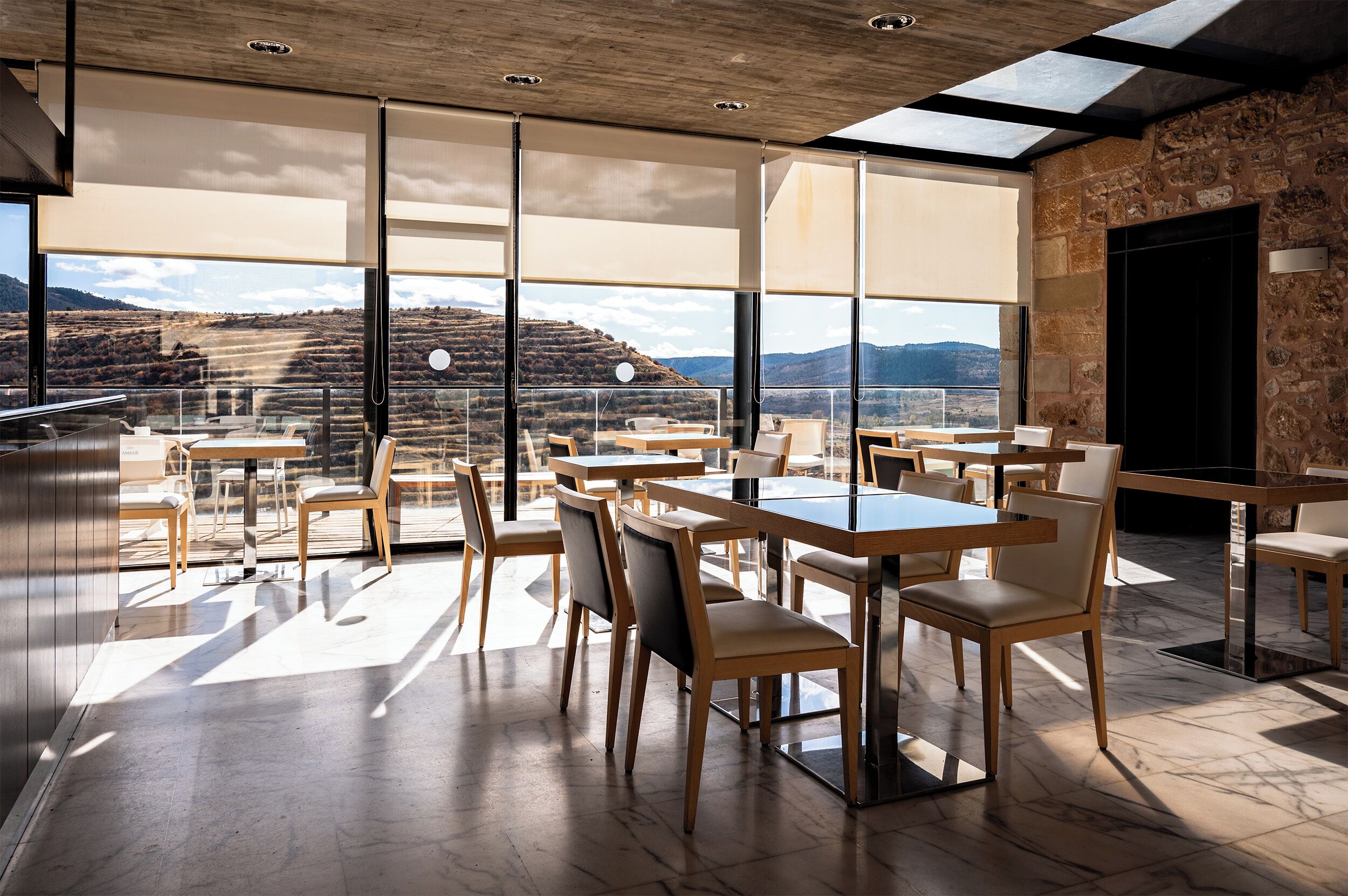 Uma sala de jantar moderna com grandes janelas, mesas e cadeiras de madeira, com vista para uma paisagem deslumbrante.