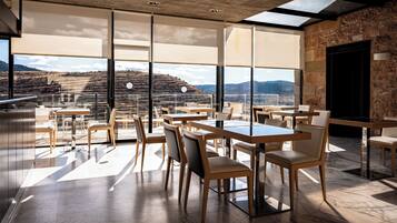 Uma sala de jantar moderna com grandes janelas, mesas e cadeiras de madeira, com vista para uma paisagem deslumbrante.