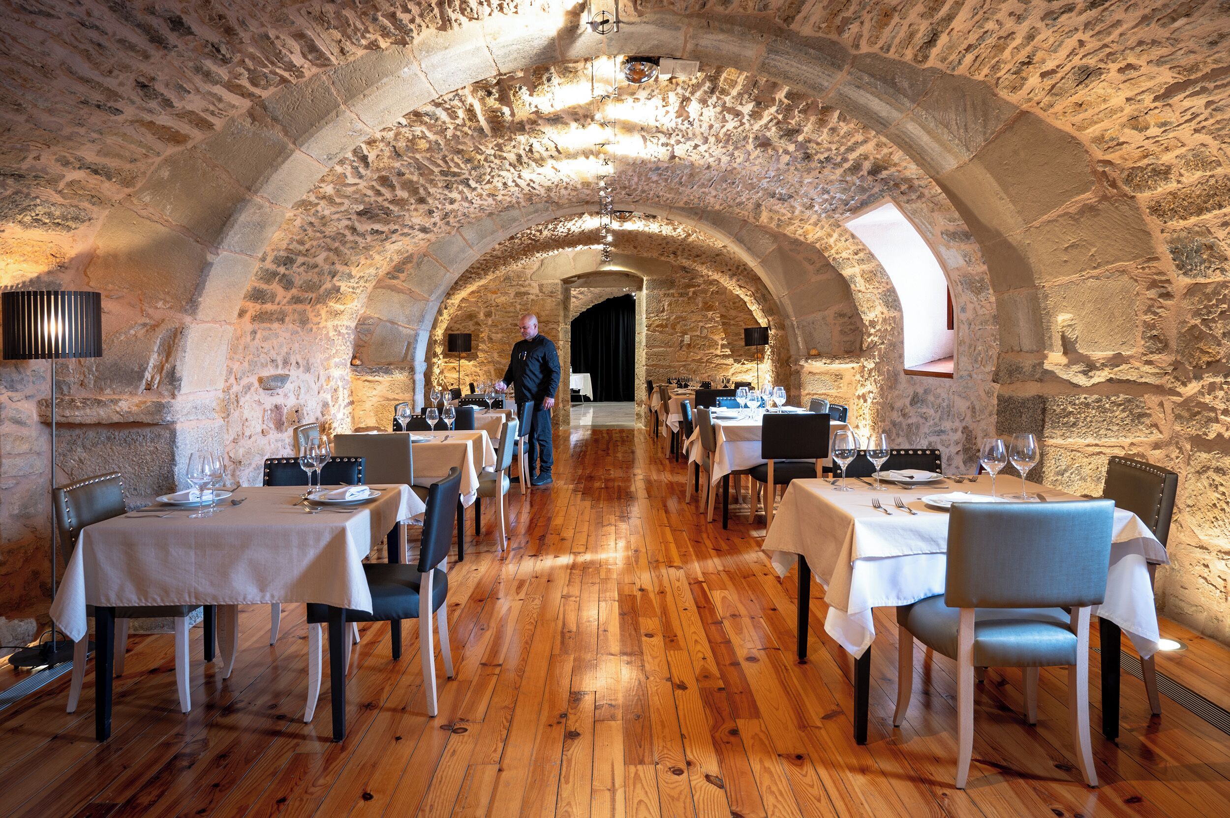 An underground dining area with stone walls and wooden floors, featuring tables set for dining.