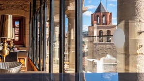 A room with large windows, a wooden ceiling, and a view of a historic building with a bell tower. - Hotel Hospedería Palacio de Allepuz (Allepuz)