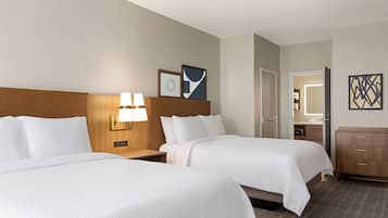 Habitación de hotel con dos camas, cabecero de madera, mesitas de noche con lámparas, cómoda y un cuadro en la pared.