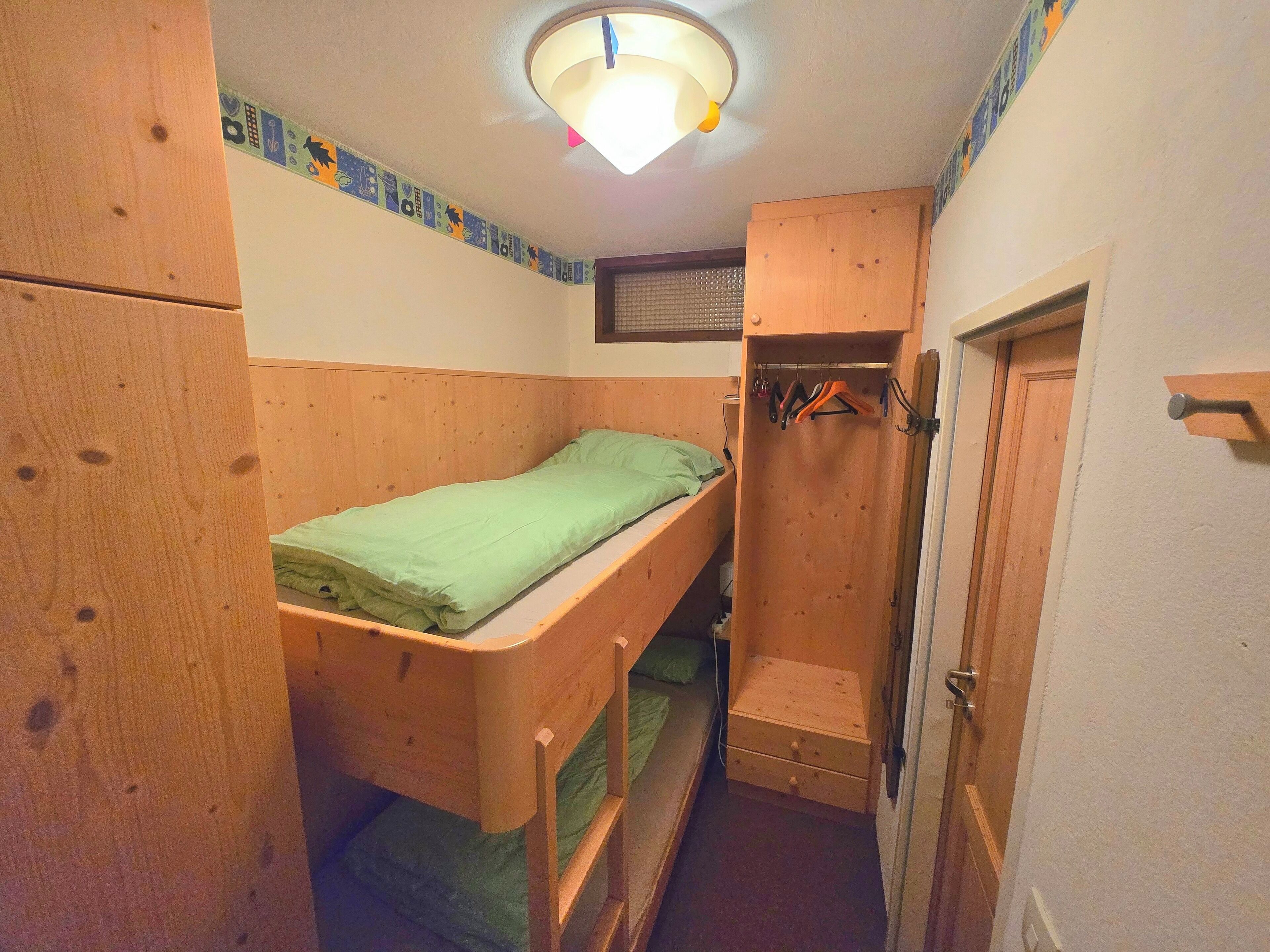 A small, compact room with a bunk bed, a wooden wardrobe, and a door.