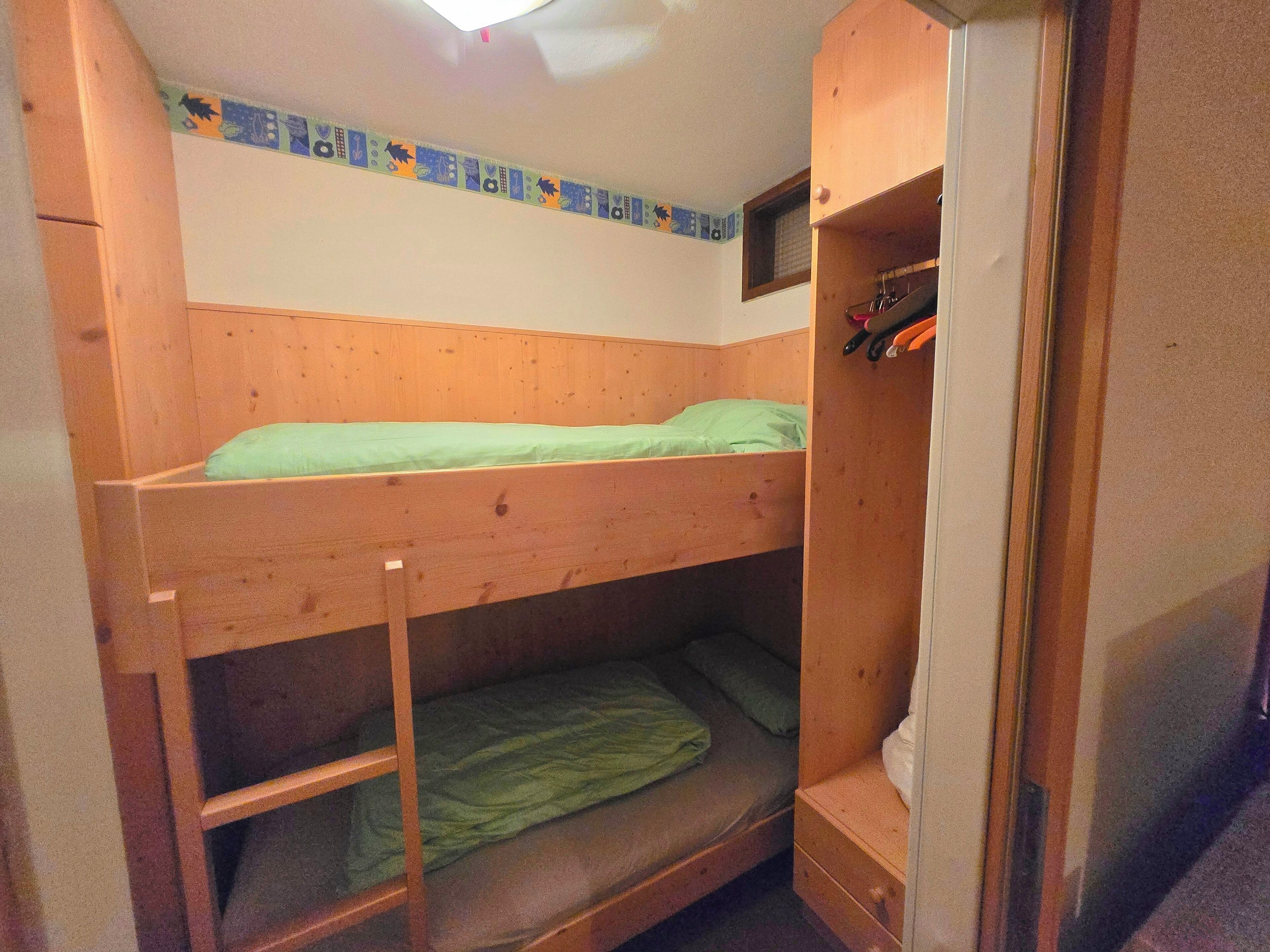 Un lit superposé avec un lit inférieur, une petite étagère avec un miroir et une fenêtre donnant sur l’extérieur.