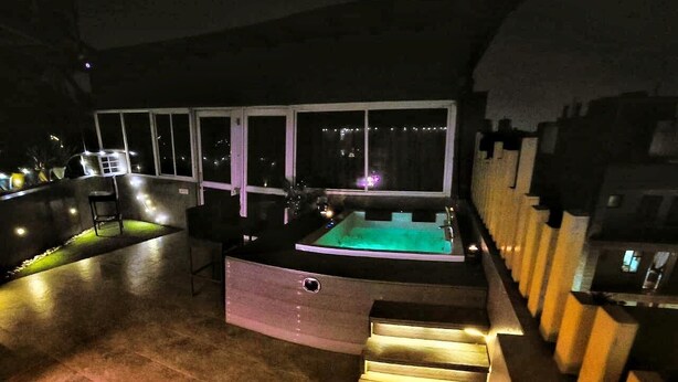 Ein Poolbereich auf dem Dach mit Whirlpool, Sitzgelegenheiten und Blick auf die nächtliche Stadt.
