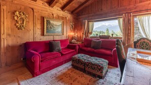 Um interior em madeira com um sofá vermelho, um banquinho estampado e uma mesa com uma cadeira.