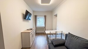 A compact living space with a kitchenette, a dining table, a sofa, and a TV mounted on the wall.