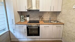 A compact kitchen with white cabinetry, a built-in oven, a stainless steel sink, and a coffee maker.