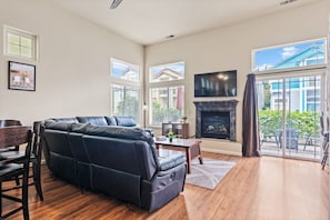 A spacious living room with a black leather sofa, a fireplace, and a large window offering a view of the outside.