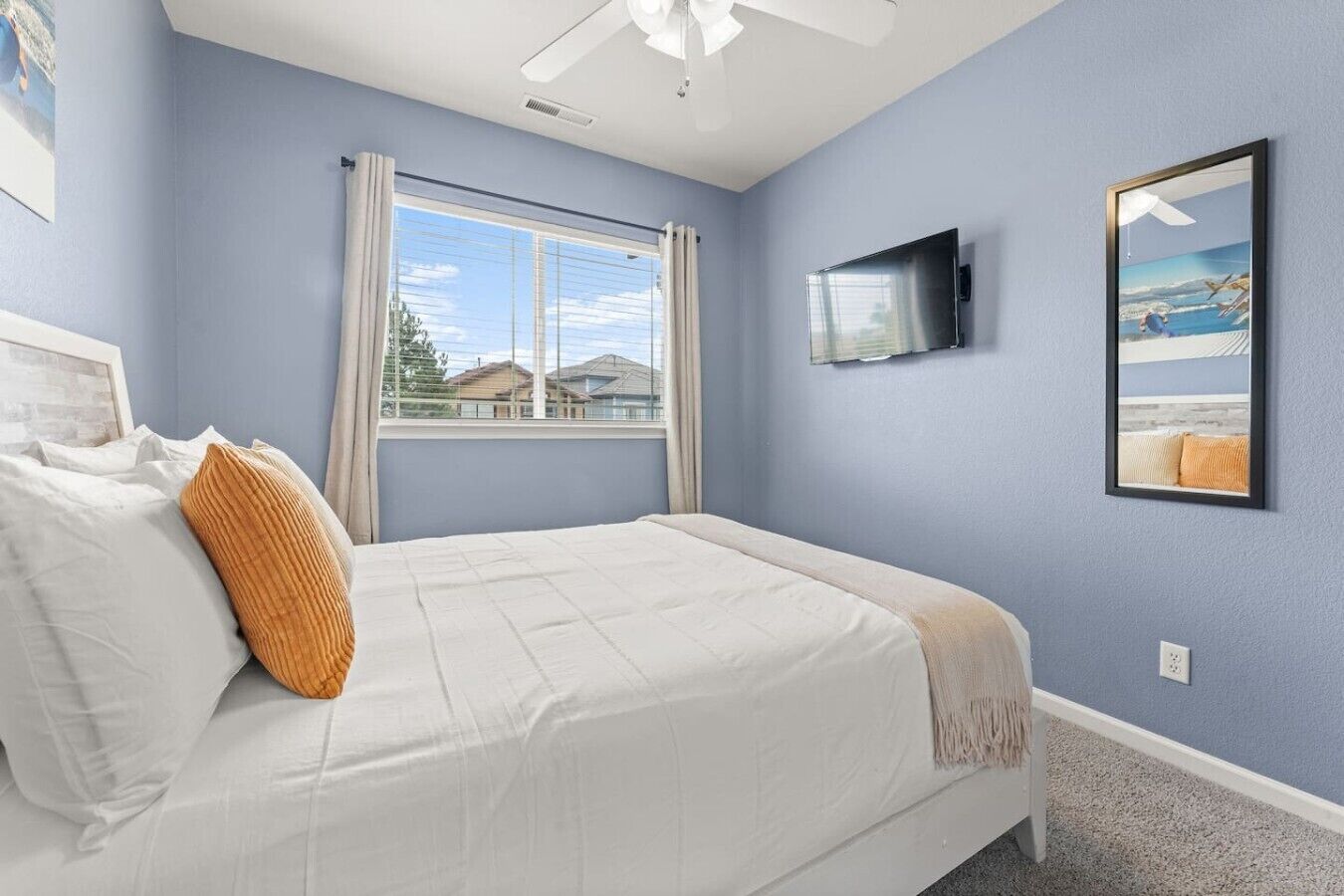 A bedroom with a bed, a window, a ceiling fan, a TV, and a framed picture on the wall.