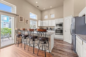 A modern kitchen with white cabinets, a stainless steel refrigerator, and a bar area with stools.