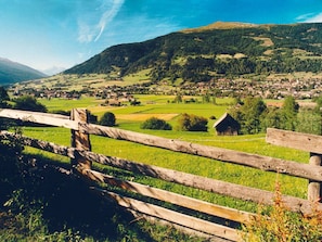Un paisaje rural con una cerca de madera, un pequeño edificio de madera y un pueblo al fondo.