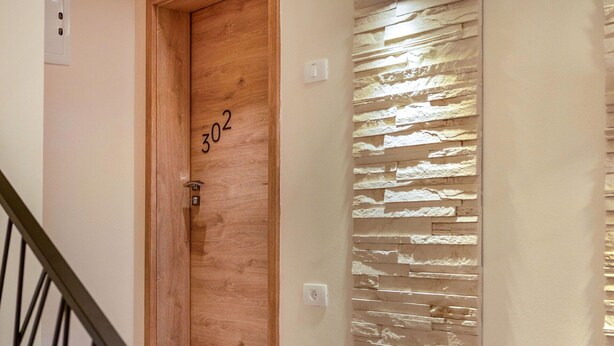 A wooden door with the number 302, a stone-textured wall, and a staircase with a metal railing. - Beautiful apartment for 4 people with A/C, WIFI, TV and panoramic view (Postojna)