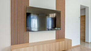 A modern living room with a flat-screen TV mounted on a wooden panel wall, a wooden entertainment unit below, and a herringbone-patterned wooden floor. - Beautiful apartment for 4 people with A/C, WIFI, TV and panoramic view (Postojna)