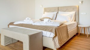 A neatly made bed with white linens and a beige headboard, a small bedside table, and a bench at the foot of the bed. - Beautiful apartment for 4 people with A/C, WIFI, TV and panoramic view (Postojna)