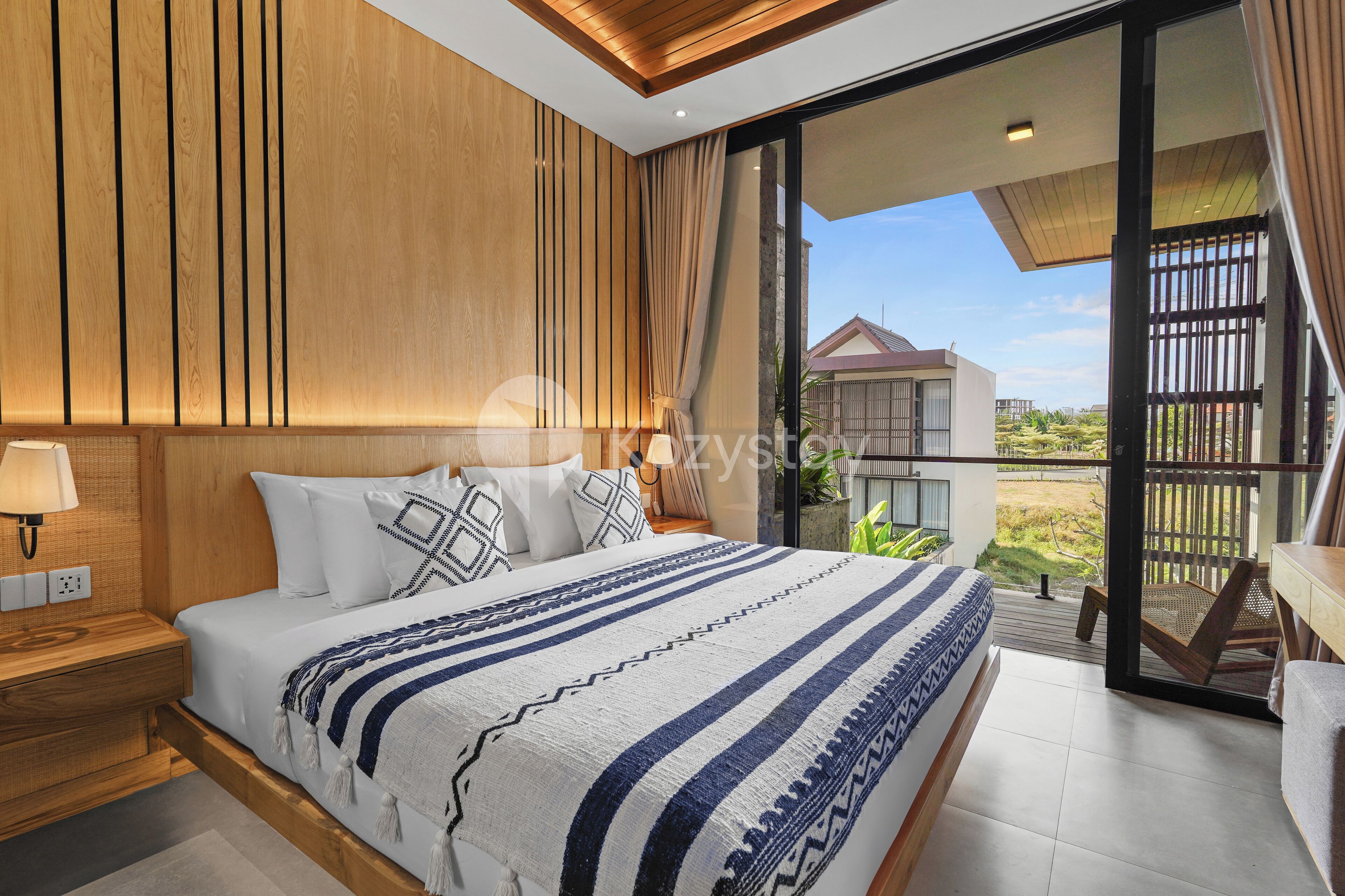 Un dormitorio moderno con una cama grande, paneles de madera, una mesita de noche y vistas al exterior a través de una puerta corrediza de vidrio.